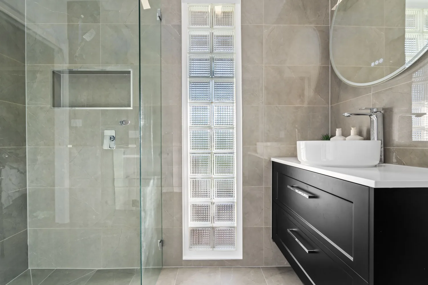 Black vanity with round mirror and grey feature tiling