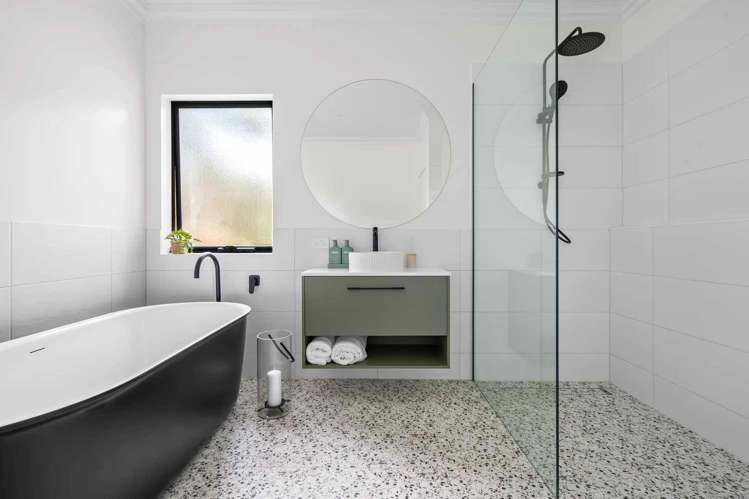 Bathroom with terrazzo floor tiling, black freestanding bath and green vanity