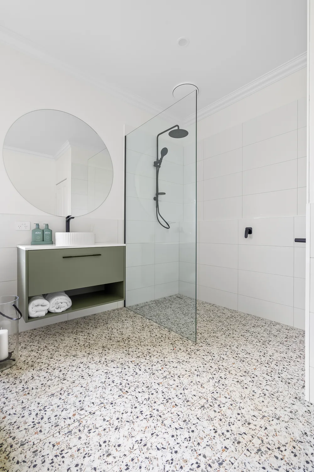 Sage-green vanity with terrazzo floor and glass walk-in shower