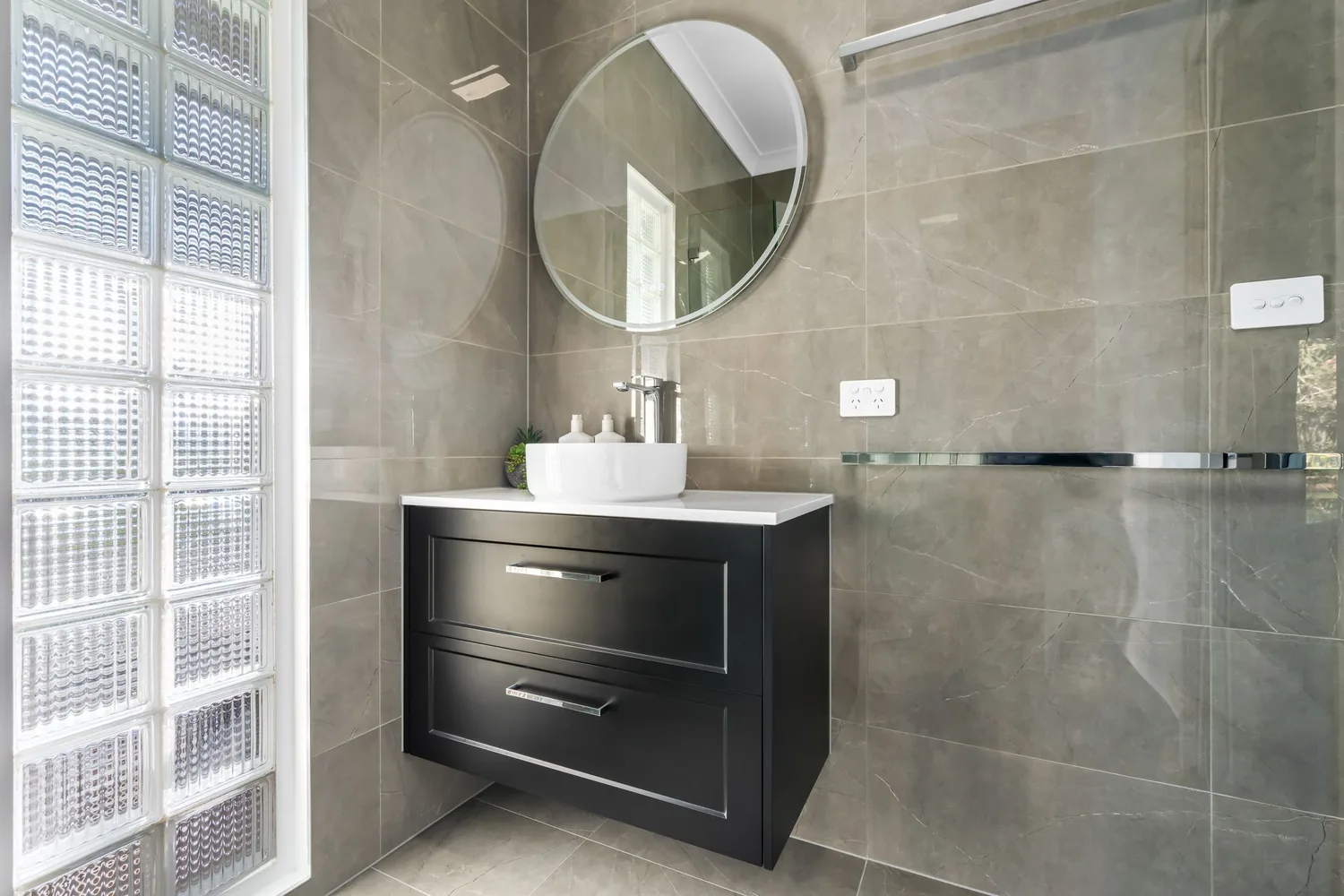 Black vanity with round mirror and grey feature tiling
