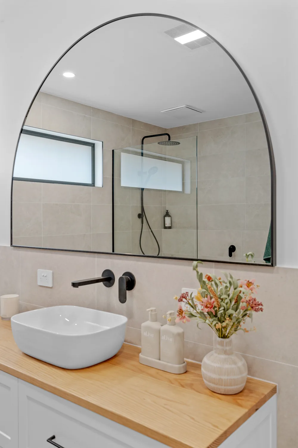 Vessel basin on timber vanity beneath a large arched mirror